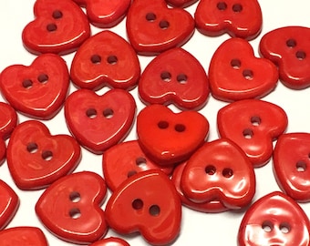 May include: A collection of red heart-shaped buttons with two holes each. The buttons are made of plastic and have a glossy finish.