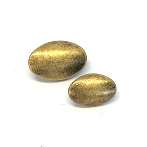May include: Two oval-shaped metal buttons in a brass finish. The larger button is slightly larger than the smaller button.