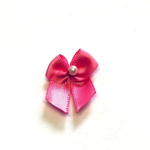 May include: A small pink satin bow with a pearl in the centre.