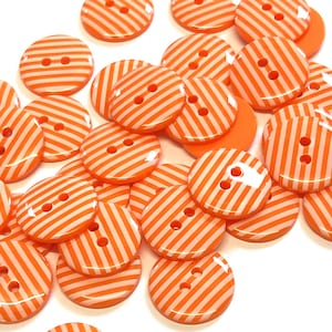 Könnte beinhalten: Eine Sammlung von orangefarbenen und weißen gestreiften Knöpfen mit jeweils zwei Löchern. Die Knöpfe sind aus Kunststoff und haben eine glänzende Oberfläche.