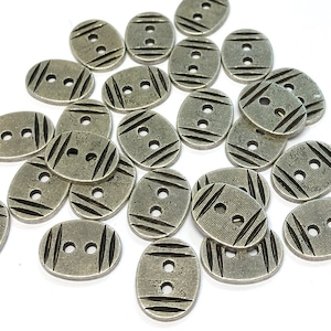 May include: A collection of oval-shaped metal buttons with a textured surface and two holes. The buttons are silver in color and have a slightly distressed look.
