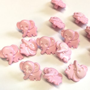 Pode incluir: Uma coleção de botões de plástico rosa em forma de elefante. Os botões têm um design em relevo e são perfeitos para adicionar um toque de fantasia a qualquer projeto.