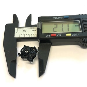 May include: A black cat button with white eyes, measuring 21.0 mm in diameter, as shown on a digital caliper.