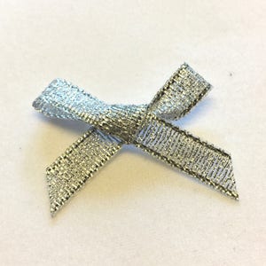 May include: A silver bow made of shimmery ribbon. The bow is tied in a simple knot and has a slightly frayed edge.