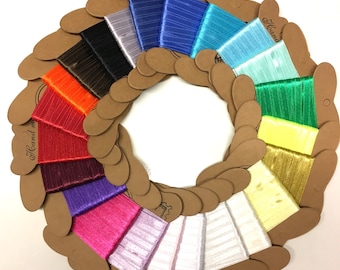 May include: A variety of colours of hand-wound embroidery floss spools arranged in a circle. The spools are made of cardboard and have a label that says "Hand Wound".