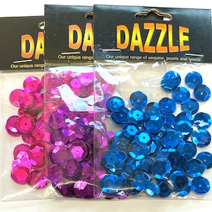 May include: Three bags of sequins, pearls, and beads. The bags are labeled "DAZZLE" and feature a variety of colors, including pink, purple, and blue.