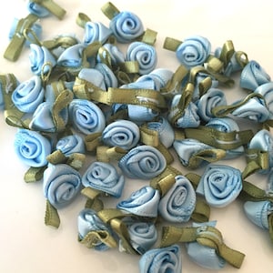 Peut inclure: Une collection de roses en ruban de satin bleu clair avec des accents de ruban vert. Les roses sont petites et délicates, parfaites pour ajouter une touche d'élégance aux travaux manuels et aux projets.