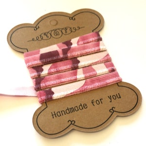 May include: Pink and white patterned elastic ribbon wound around a brown card with the text "Handmade for you".