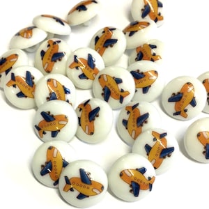 May include: A collection of white round buttons with a yellow airplane design. The airplanes have blue details and are outlined in black.
