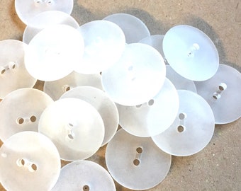 May include: A pile of white plastic buttons with two holes each. The buttons are round and smooth.