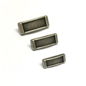 May include: Three silver metal rectangular buttons with a textured surface. The buttons are arranged in a vertical stack, with the largest button at the top and the smallest button at the bottom.