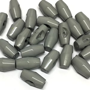 以下が含まれることがあります： 灰色のプラスチック製のトグルボタンの山。ボタンは楕円形で、中央に穴が開いています。