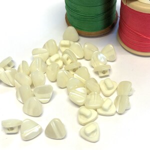 May include: A group of white triangle-shaped buttons with a white shank. The buttons have a pearlescent finish and a subtle striped pattern.