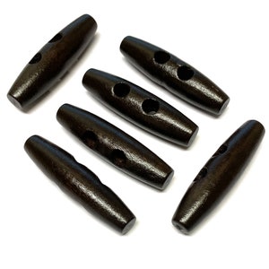 Könnte beinhalten: Sechs dunkelbraune Holz-Toggle-Knöpfe mit jeweils zwei Löchern. Die Knöpfe sind oval geformt und haben eine glatte Oberfläche.