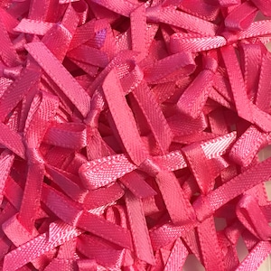 May include: A collection of small, bright pink satin ribbon bows. The bows are closely arranged, forming a textured surface. Each bow is knotted in the middle, and the ribbon has a subtle sheen.