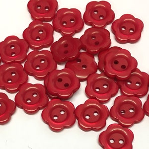 May include: A collection of red plastic flower-shaped buttons with two holes each.
