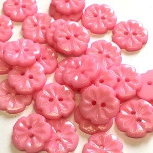 Könnte beinhalten: Eine Sammlung von rosa Plastikknöpfen in Blütenform mit jeweils zwei Löchern. Die Knöpfe haben eine glänzende Oberfläche.