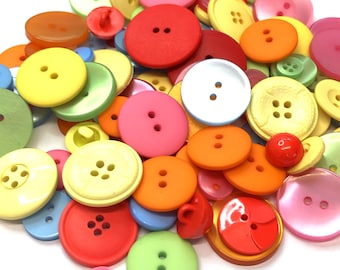 Puede incluir: Una gran colección de botones de plástico de colores en varios tamaños y formas. Los botones son una mezcla de rojo, naranja, amarillo, verde, azul, rosa y blanco.