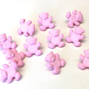 Könnte beinhalten: Eine Sammlung von 12 rosa Plastik-Teddybär-Knöpfen. Die Knöpfe haben einen Durchmesser von etwa 2,5 cm und eine strukturierte Oberfläche.