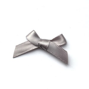 May include: A small, gray satin bow. The bow is tied in a simple knot and has a slightly textured surface.
