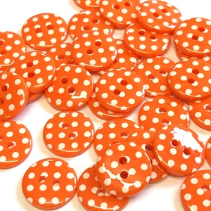 May include: A pile of orange buttons with white polka dots. The buttons are round and have two holes.