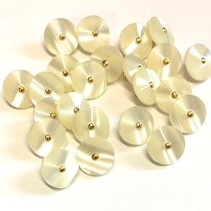 May include: A collection of 20 white, round, flat buttons with a gold centre. The buttons have a slightly iridescent finish.