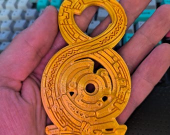 May include: A 3D printed golden yellow infinity symbol with intricate details and a circular design in the center.