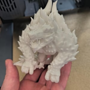 Può includere: Una statuetta bianca stampata in 3D di una creatura con la schiena spinosa e un'espressione feroce.