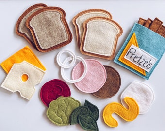 May include: Felt food play set with various food items including bread, cheese, pretzels, and vegetables. The set is perfect for pretend play and imaginative learning.