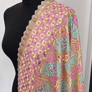 May include: A rectangular shawl featuring a gold base fabric with intricate embroidery in pink, light blue, and gold thread. The design includes geometric square patterns, small circular mirrors, and tiny gold sequins, finished with a scalloped lace trim.