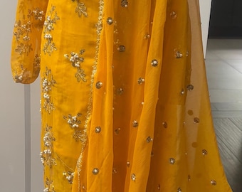 May include: A vibrant yellow salwar kameez ensemble. The outfit features intricate embroidery and embellishments, including pearls and sequins. The sheer dupatta drapes elegantly, showcasing the detailed craftsmanship of the traditional Indian attire.