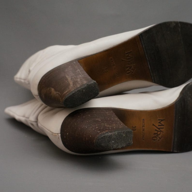 Puede incluir: Botas de cuero blanco roto con tacones de madera apilados. Las suelas est&aacute;n marcadas con "MYRG" y "MADE IN ITALY", talla 38. Las botas est&aacute;n en &aacute;ngulo, mostrando los detalles del tal&oacute;n y la suela.