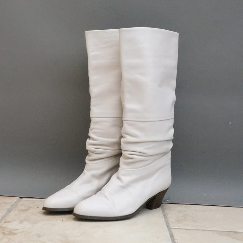 Puede incluir: Un par de botas altas de color blanco roto. Las botas tienen un dise&ntilde;o holgado con una textura ligeramente arrugada. Cuentan con una puntera redondeada y un tac&oacute;n de bloque marr&oacute;n oscuro.