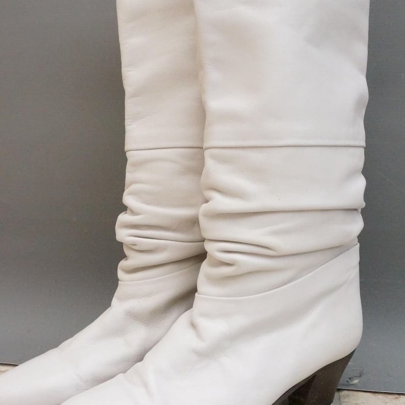 Puede incluir: Un par de botas blancas de cuero hasta la rodilla. Las botas tienen un dise&ntilde;o holgado con un tac&oacute;n apilado. El cuero parece suave y las botas est&aacute;n en buen estado.