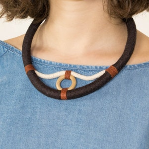 Può includere: Una collana di corda marrone, bianca e beige con un accento ad anello di legno.