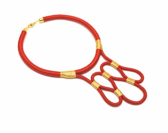 May include: A red and gold necklace made of woven cord. The necklace has a simple choker style with a decorative pendant that features multiple loops.