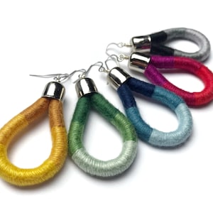 Könnte beinhalten: Fünf Paar bunte, handgefertigte, mit Garn umwickelte Ohrringe mit silbernen Haken. Die Ohrringe sind in einem Regenbogenfarbton, beginnend mit Gelb und Orange, dann Grün und Blau, dann Blau und Türkis, dann Pink und Rot und schließlich Schwarz und Grau.