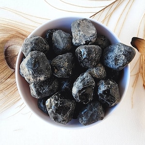 May include: A bowl filled with black obsidian tumbled stones. The stones are smooth and have a shiny, glassy finish.