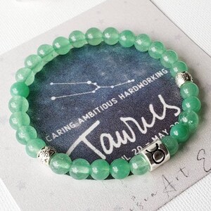 May include: Green gemstone bracelet with a silver charm featuring the Taurus zodiac symbol and the text "Taurus, Caring, Ambitious, Hardworking, April 20 - May 20".