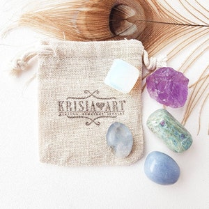 May include: A set of five tumbled stones in a small burlap bag. The stones are amethyst, clear quartz, blue lace agate, and two shades of blue aventurine. The bag has a label that says "KrislaArt".