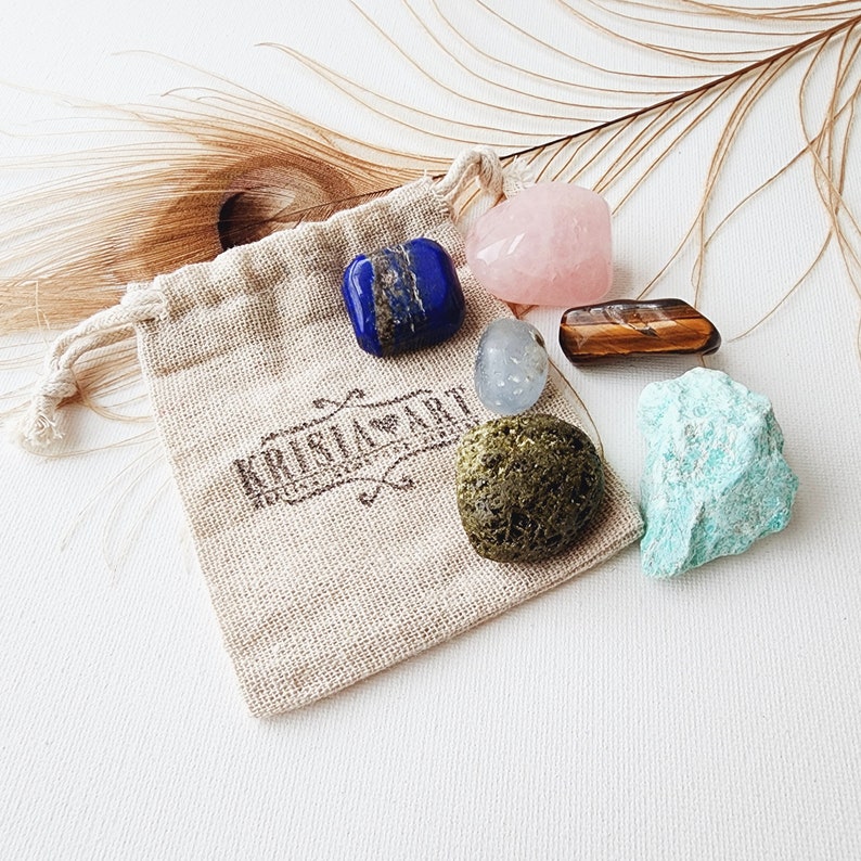 May include: A small pouch containing six tumbled crystals: blue lapis lazuli, pink rose quartz, brown tiger's eye, light blue aquamarine, green aventurine, and green amazonite.