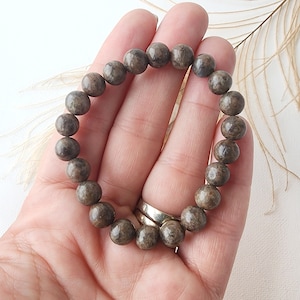 May include: A brown and gray beaded bracelet with round beads. The bracelet is made of natural stone and has a rustic look.