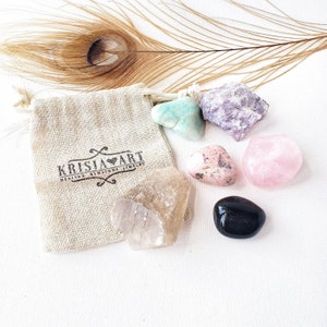 Puede incluir: Un conjunto de siete cristales pulidos en una peque&ntilde;a bolsa de arpillera. Los cristales son de color rosa, verde, morado, transparente y negro. La bolsa tiene el texto "Krisia Art Healing Crystals Jewelry" impreso en ella.
