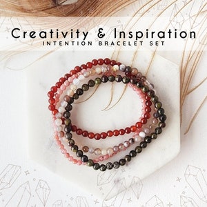 May include: Set of four beaded bracelets in red, pink, green, and white. The bracelets are stacked on a white surface and feature the text "Creativity & Inspiration Intention Bracelet Set".