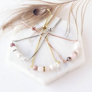 May include: Five adjustable bracelets with a variety of gemstone beads, including white, pink, and gray. The bracelets are made with a silver, gold, and rose gold chain.