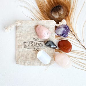 May include: A set of six tumbled crystals in a small burlap pouch. The crystals are pink, white, purple, black, and red. The pouch has the text "Krisla Yar" printed on it.