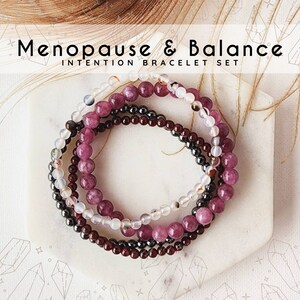 May include: Set of four bracelets with pink, white, and dark red beads. The bracelets are stacked on top of each other and say "Menopause & Balance Intention Bracelet Set".