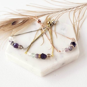 May include: Three adjustable gemstone bracelets with silver, gold, and rose gold chains. Each bracelet features a variety of semi-precious stones, including amethyst, clear quartz, and green aventurine.