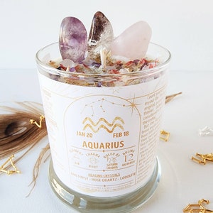 May include: A glass candle jar with a white label featuring the zodiac sign Aquarius, dates January 20 to February 18, and the text "Element: Air, Chakra: Root, Ruled by: Saturn Uranus, Number: 12, Healing Crystals: Amethyst, Rose Quartz, Lodolilte". The jar is filled with a white candle and topped with amethyst, clear quartz, and rose quartz crystals.
