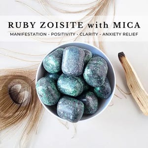 May include: A white bowl filled with polished, tumbled ruby zoisite stones with mica inclusions. The stones are mottled green and dark red. Text overlay reads: RUBY ZOISITE with MICA. MANIFESTATION - POSITIVITY - CLARITY - ANXIETY RELIEF.